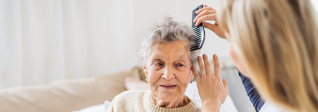 yolo-1080x380-2 An elderly woman getting her hair combed by a caretaker
